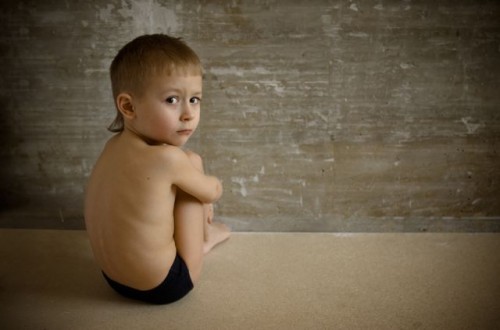 The little boy sits in a room about a wall. It sad.